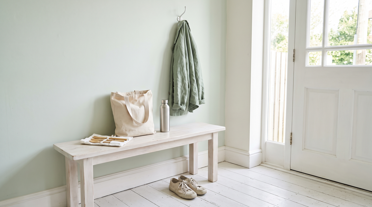 A bright entryway with a canvas tote and steel water bottle on a whitewashed bench, a sage linen jacket on a hook by the door