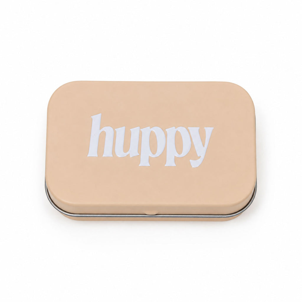 A closed, beige rectangular tin with "huppy" printed in white lowercase letters on the lid, on a white background.