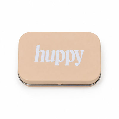 A closed, beige rectangular tin with "huppy" printed in white lowercase letters on the lid, on a white background.