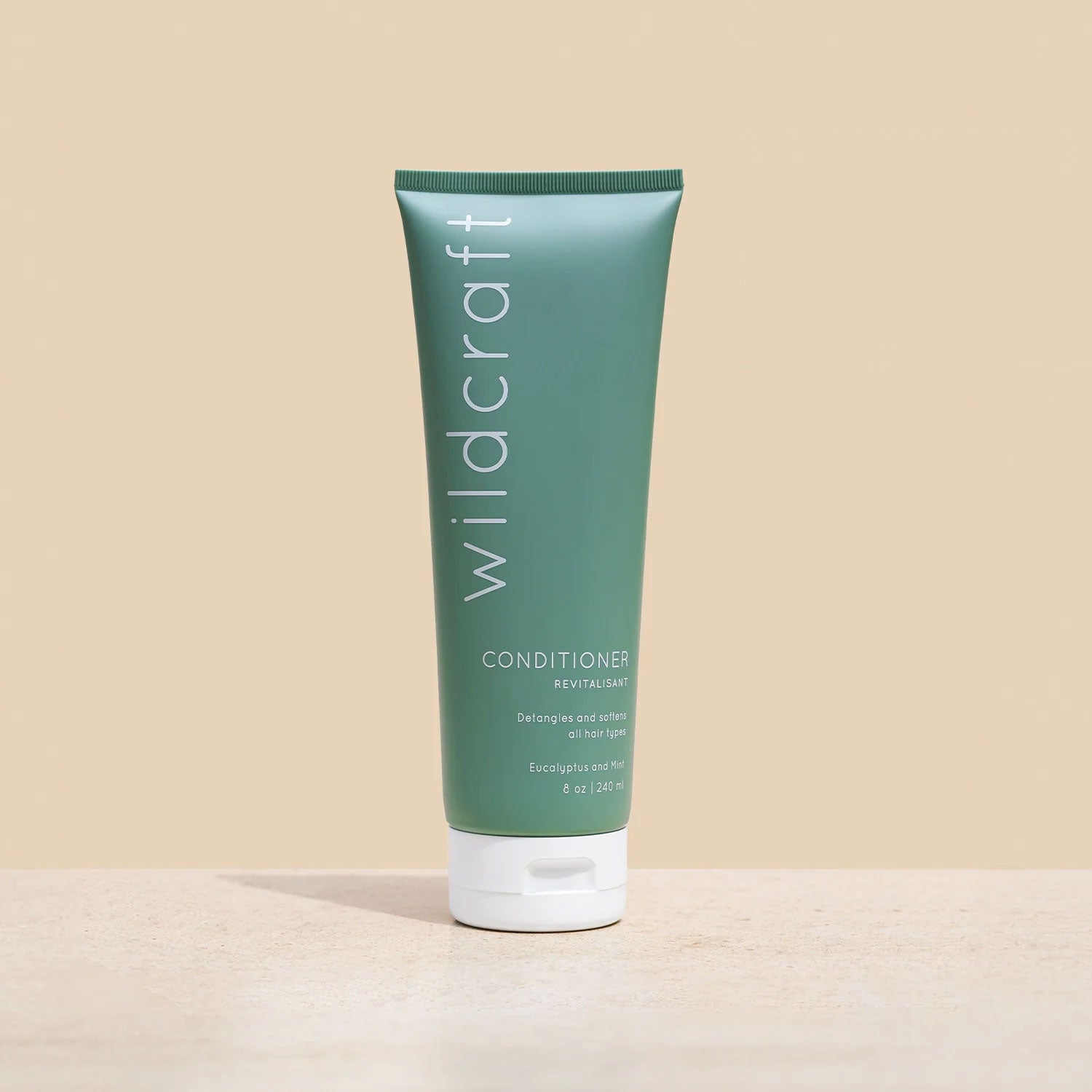 A green tube of Wildcraft conditioner stands upright on a beige stone surface.