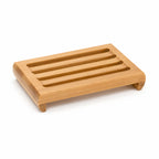 Angled side view of the slotted bamboo soap dish on a white surface, showing curved corner feet.