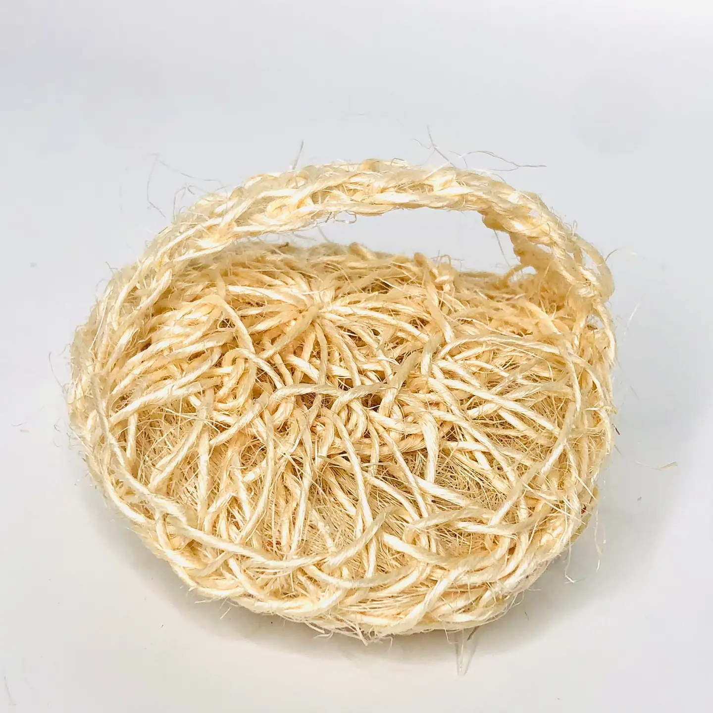 Round sisal body scrubber on a white surface, shown from the back to display the woven hand strap.