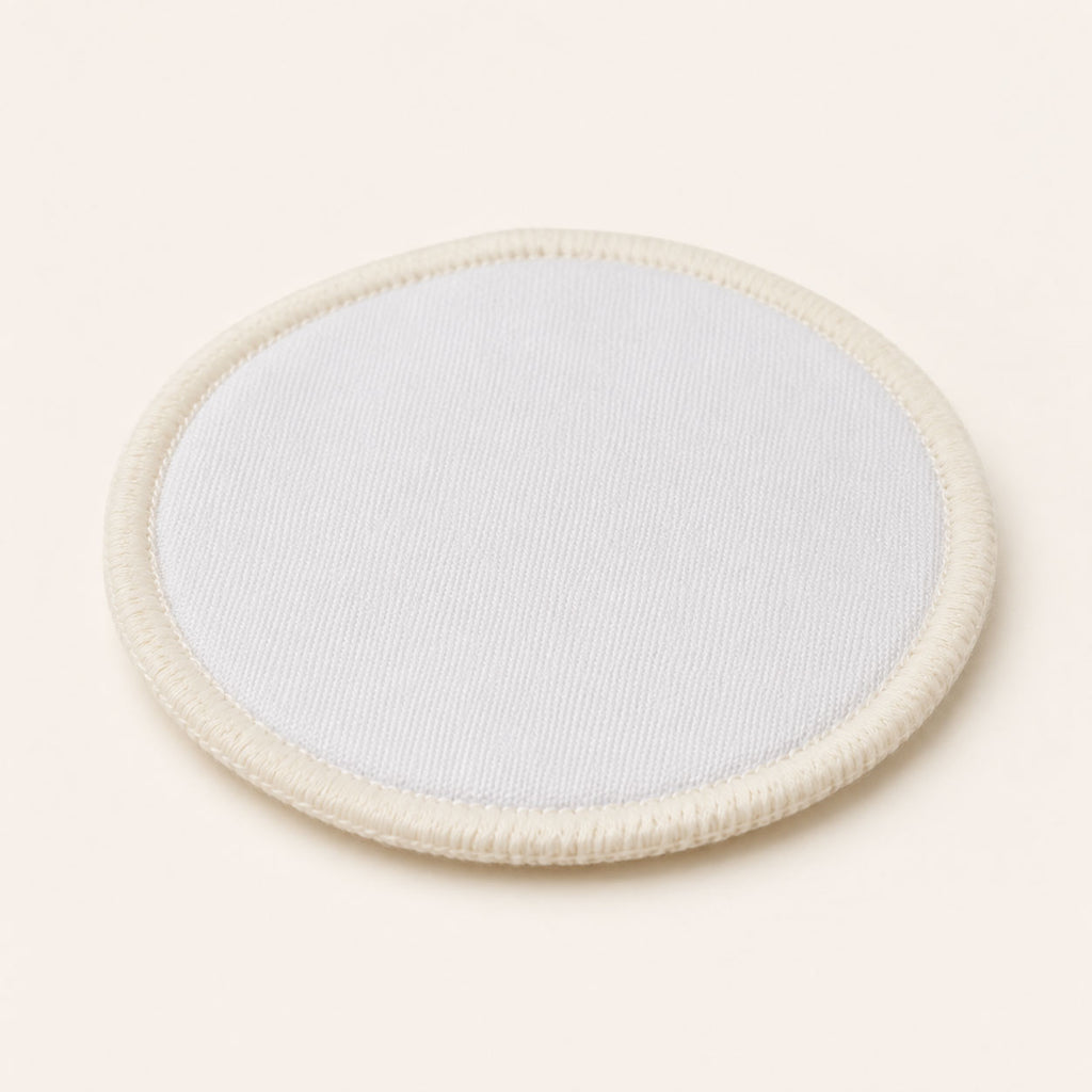 Single circular white reusable cotton makeup pad with stitched edge on an off-white background.