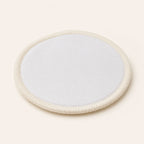 Single circular white reusable cotton makeup pad with stitched edge on an off-white background.