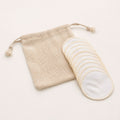 Stack of reusable white cotton pads fanned out beside a beige mesh drawstring wash bag.