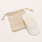 Stack of reusable white cotton pads fanned out beside a beige mesh drawstring wash bag.