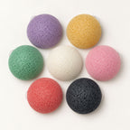 Seven colourful, dome-shaped konjac sponges arranged in a circle on a white surface, viewed from above.