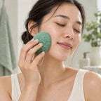 Someone with closed eyes cleansing their cheek using a green textured facial sponge.