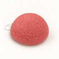 Coral-pink konjac sponge with a small white hanging string, set on a white background.