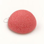 Coral-pink konjac sponge with a small white hanging string, set on a white background.