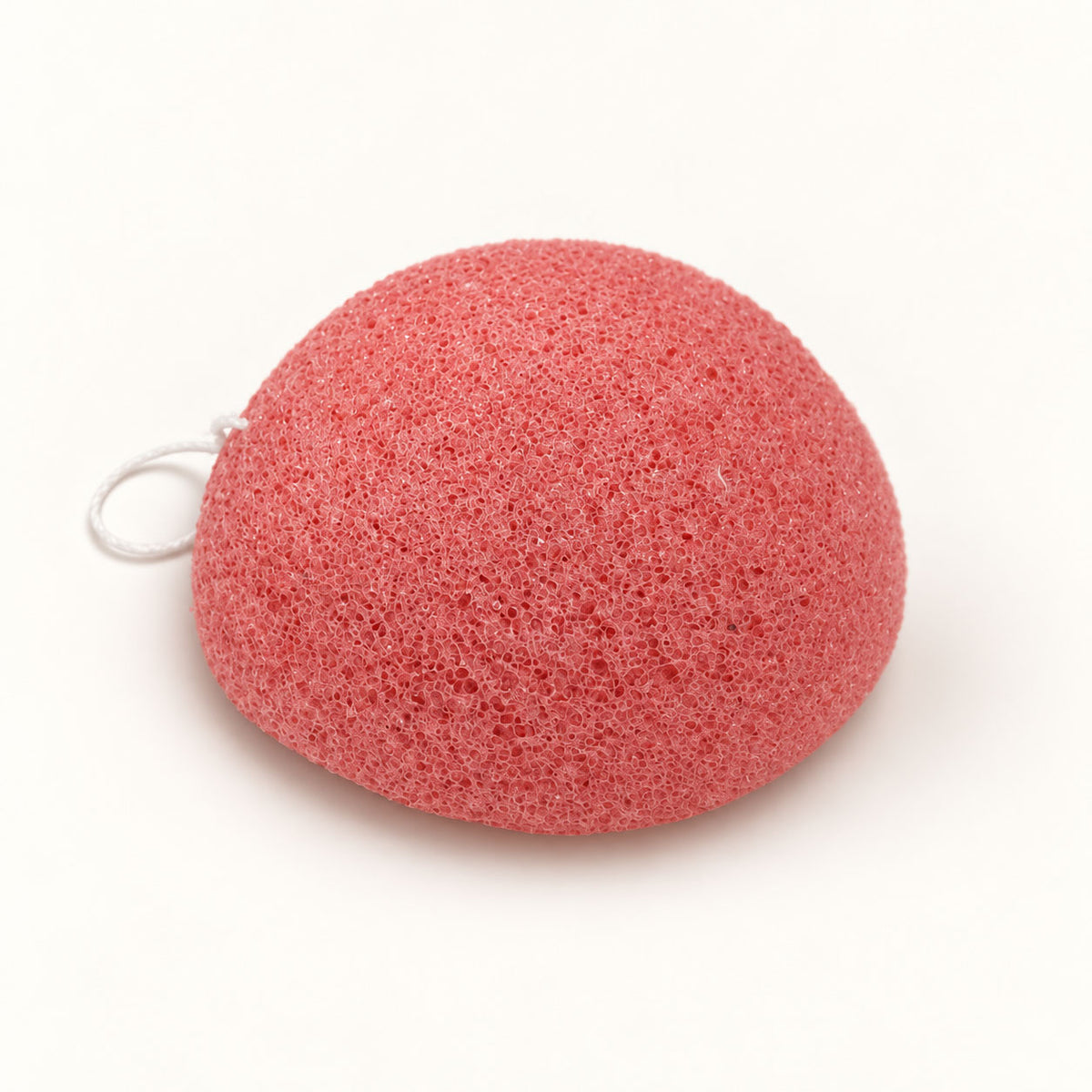 Coral-pink konjac sponge with a small white hanging string, set on a white background.