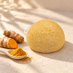 Yellow konjac sponge displayed next to fresh turmeric root and a spoonful of ground turmeric powder.
