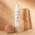 Carina Organics citrus conditioner raised on a stone plinth with a bamboo wide-tooth comb leaning behind it and an ekö + co. branded clay pink scalp massager resting in front