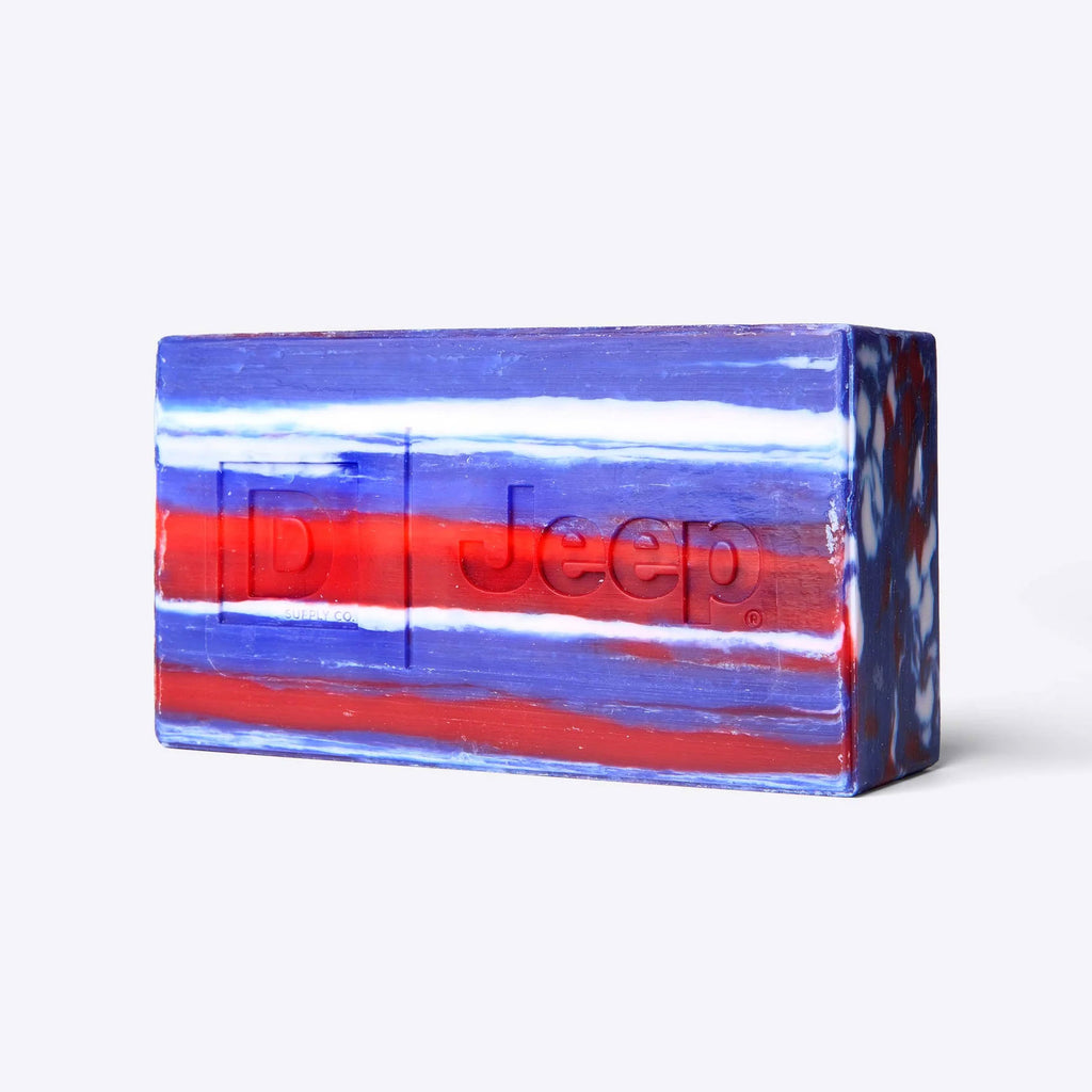 Close-up of the triple-milled Duke Cannon Jeep brick of soap with red, white, and blue marbled stripes and embossed D and Jeep® logos