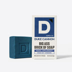 Dark blue Duke Cannon soap bar stamped with a D next to its white and blue Naval Diplomacy packaging box.