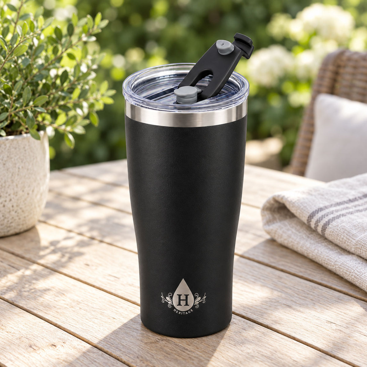 Matte black Heritage tumbler with flip-back spout lid open on an outdoor patio table