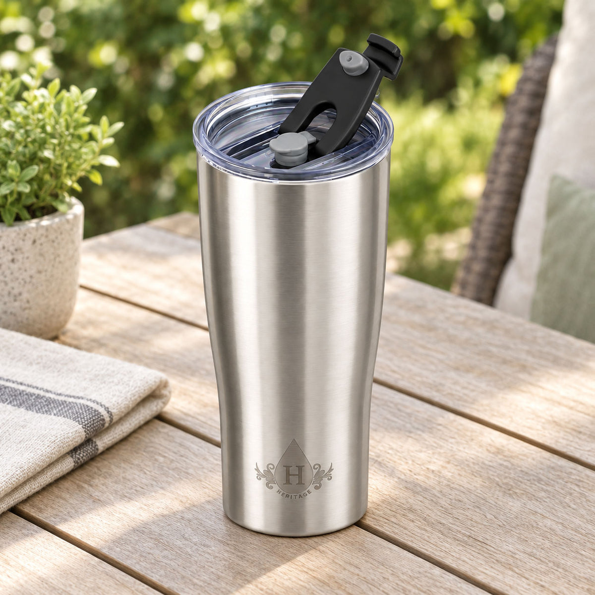 Brushed stainless steel Heritage tumbler with flip-back spout lid open on an outdoor patio table