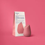 A pink, teardrop-shaped HiBAR Curl solid conditioner bar stands next to its white and pink paper carton on a pink background.