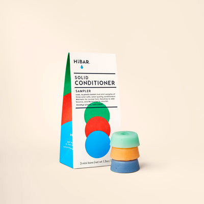 A white HiBAR sampler box next to three small, stacked solid conditioner bars in green, orange, and blue.