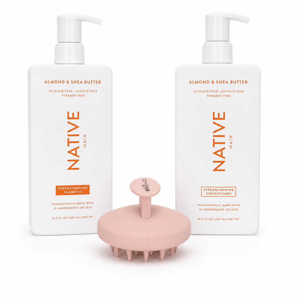 ekö + co. pale peach silicone scalp massager with visible bristles standing between Native almond and shea butter shampoo and conditioner bottles