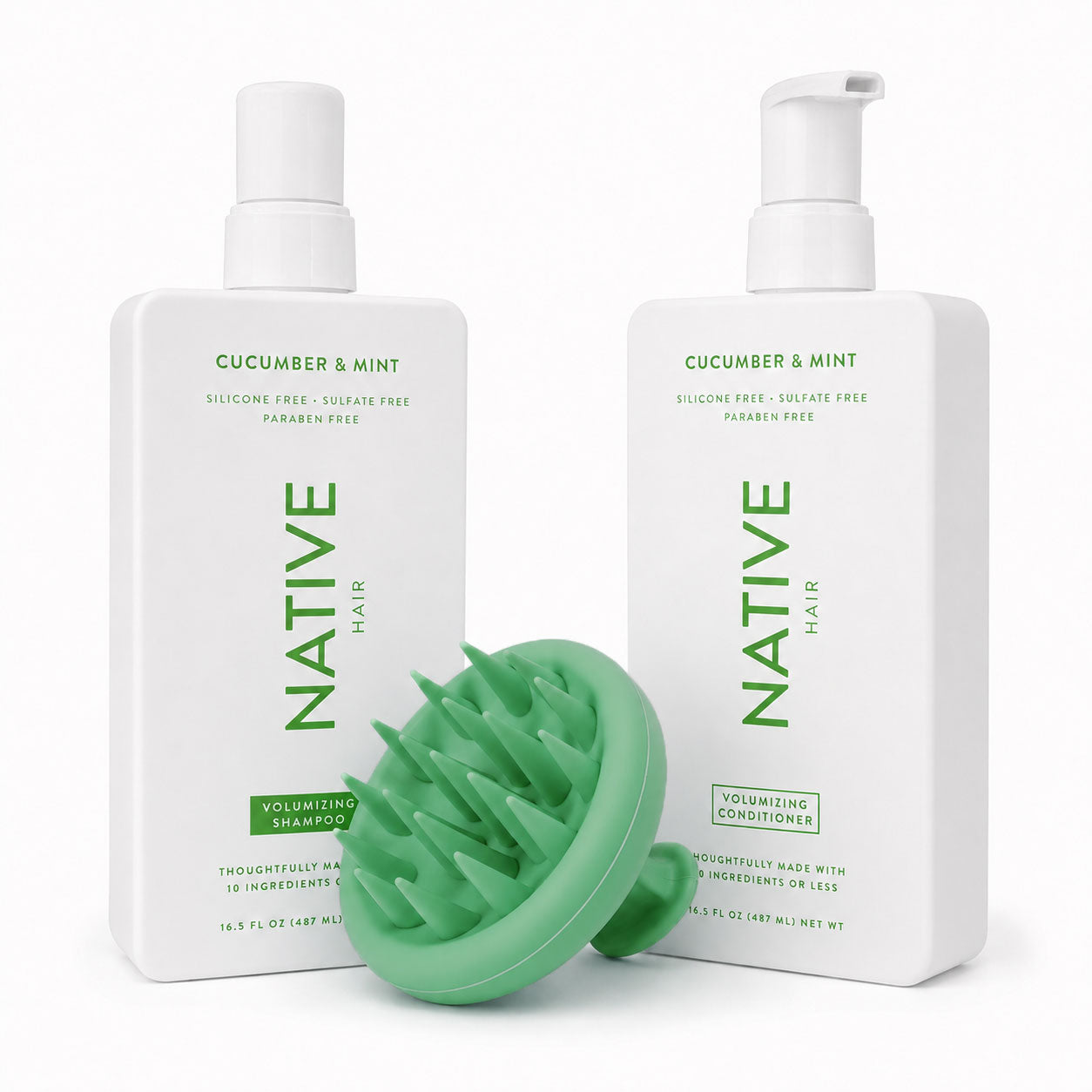 Native Cucumber and Mint volumizing shampoo and conditioner pump bottles with a green ekö + co. silicone scalp massager tilted forward between them