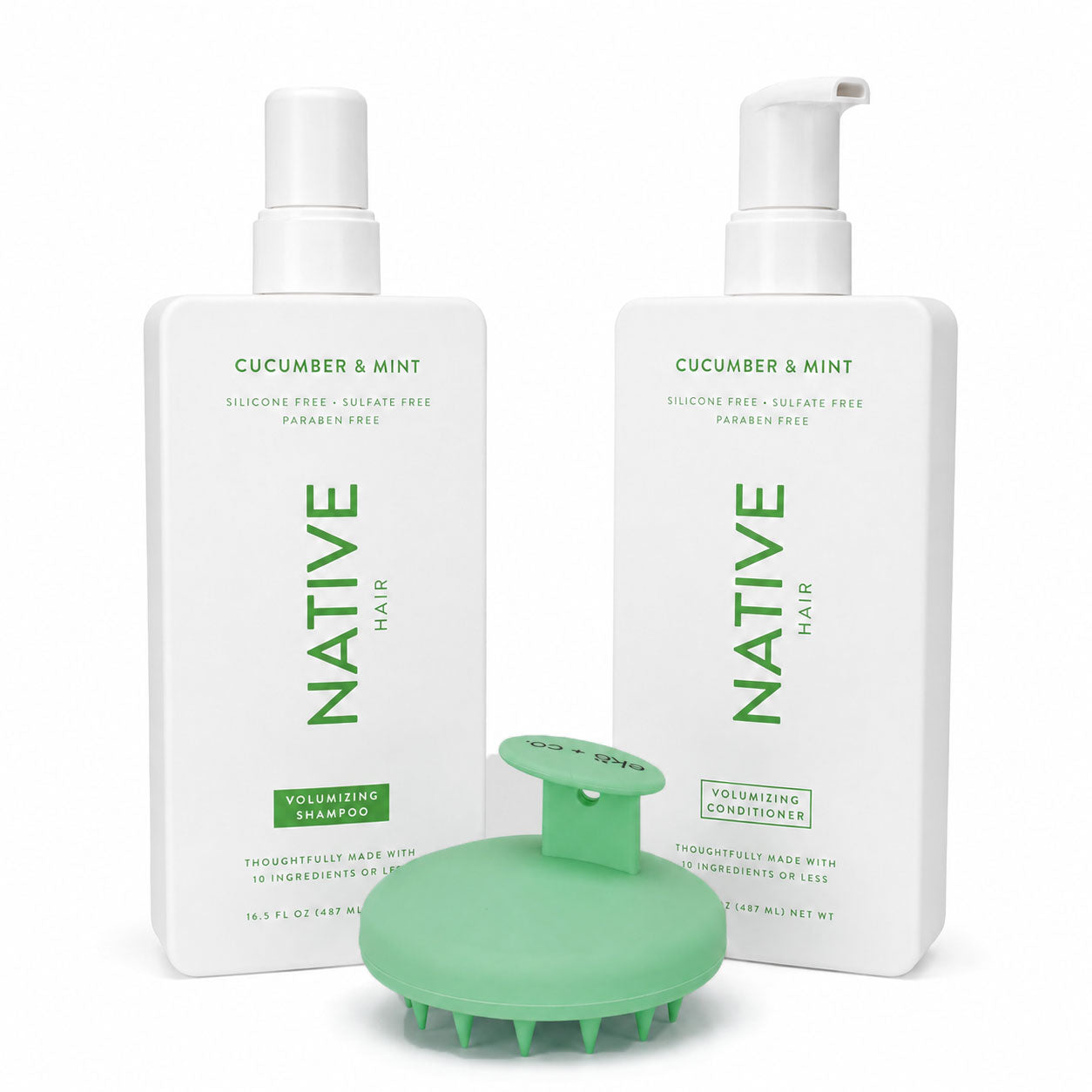 Green ekö + co. silicone scalp massager with visible bristles standing between Native cucumber and mint volumizing shampoo and conditioner bottles