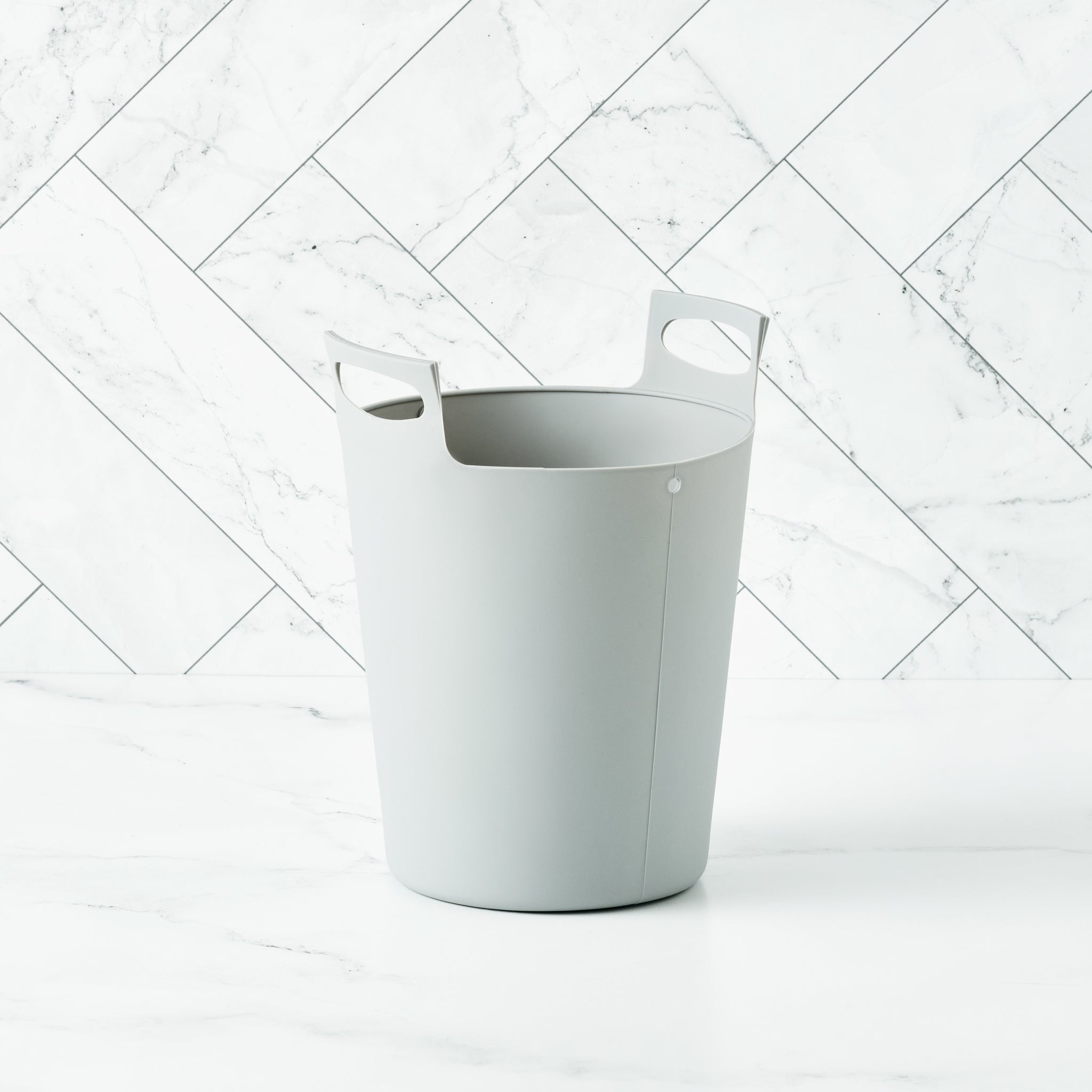 A grey Bamboozle Martha Stewart silicone liner bag for a compost bin, set on a marble surface.