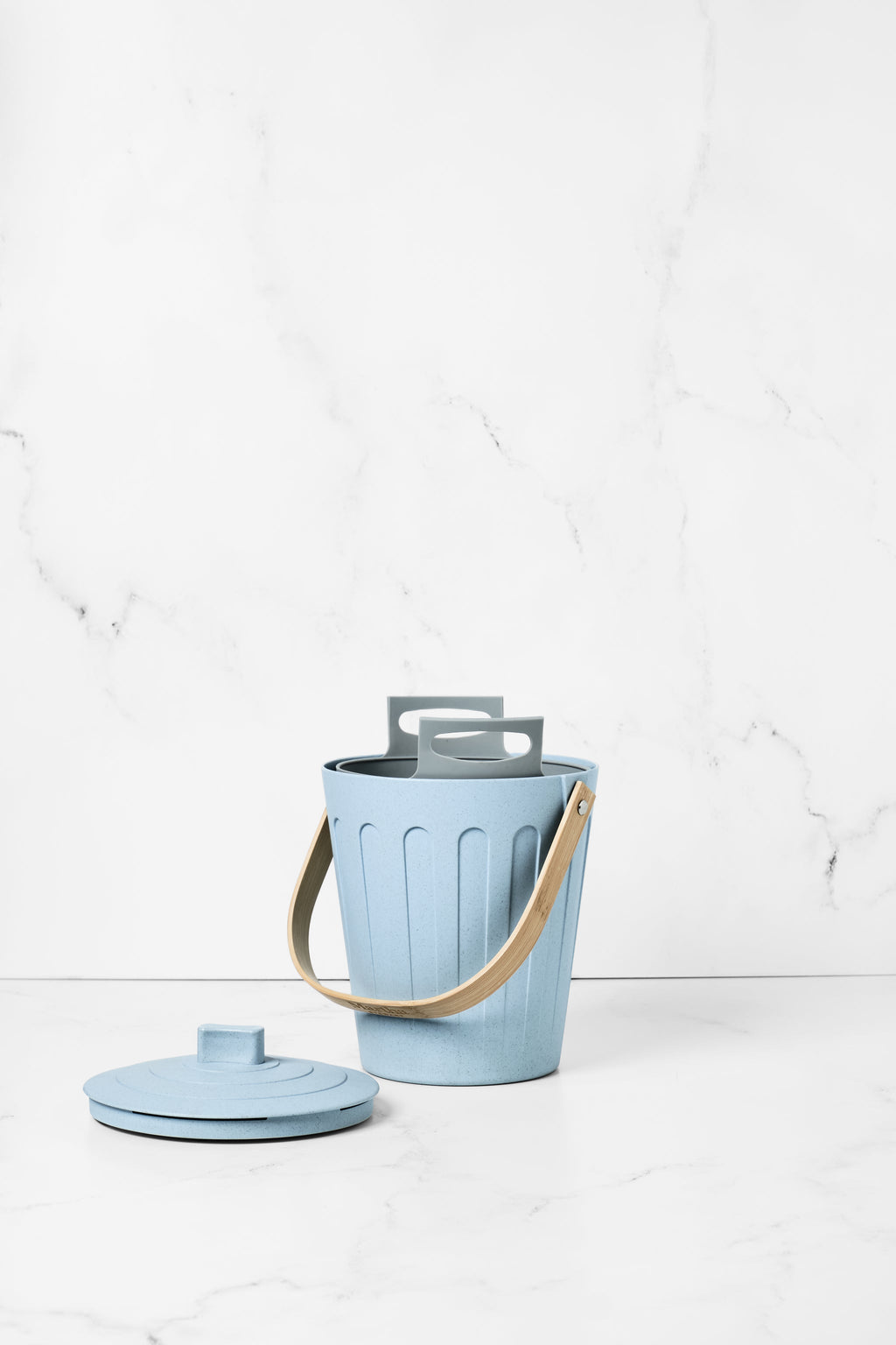 Grey Bamboozle Martha Stewart silicone liner bag inside a light blue compost pail with a wooden handle and lid nearby.