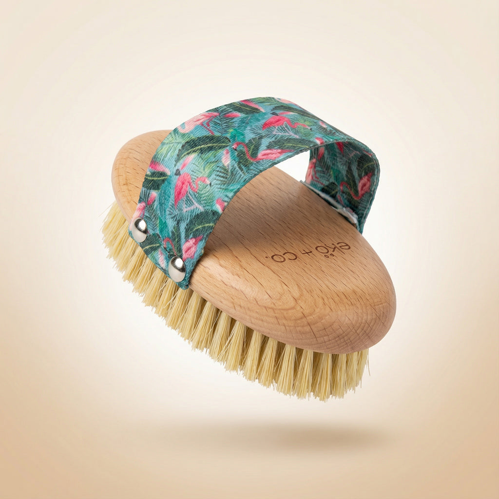 dry body brush shown at angle displaying natural sisal bristles and beechwood handle with flamingo strap arched over top