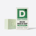 Pale green soap bar embossed with a letter D, standing beside its white and green Duke Cannon box.