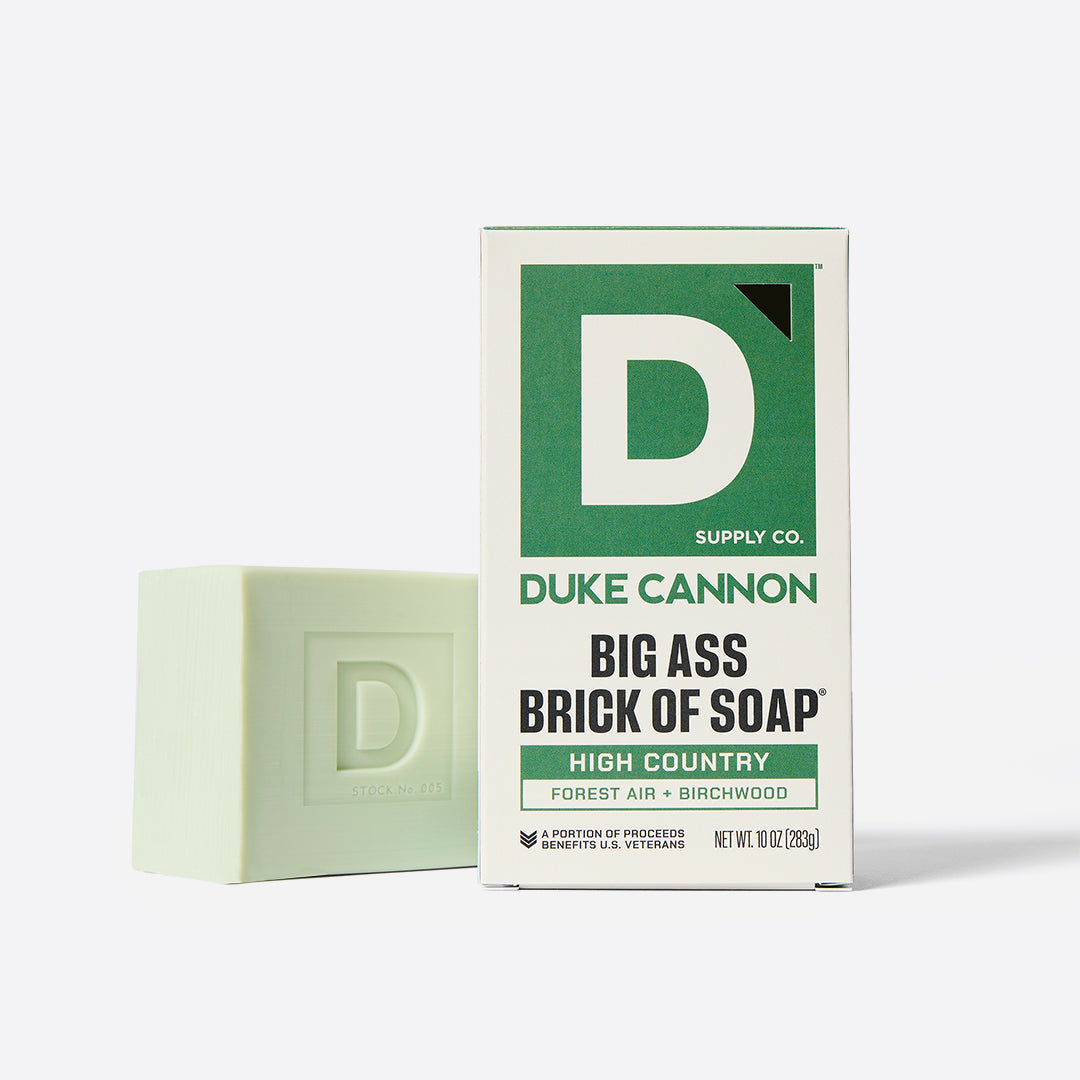 Pale green soap bar embossed with a letter D, standing beside its white and green Duke Cannon box.