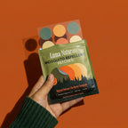 Hand holding a green Luna Naturals patch pouch, pulling out a sheet of round stickers on an orange background.