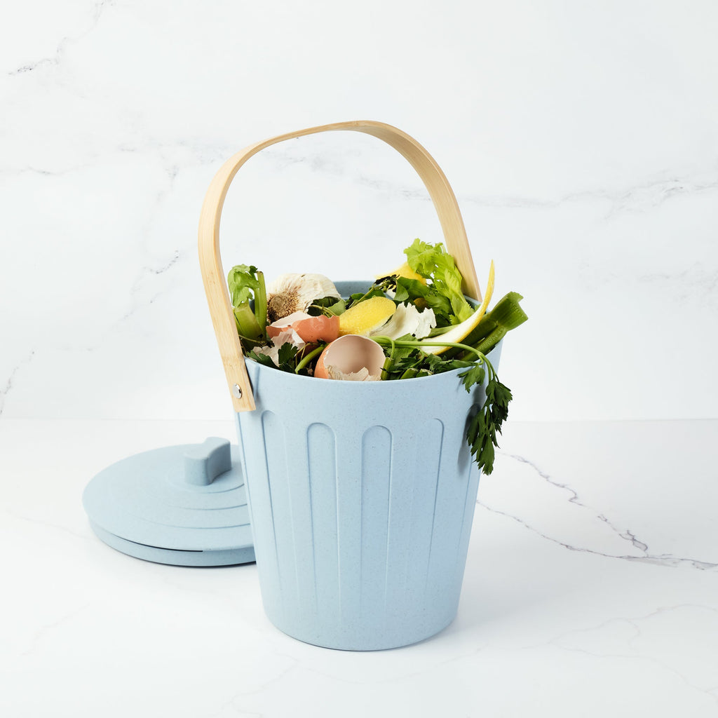 Martha Stewart light blue indoor compost bin filled with vegetable scraps on a marble countertop.