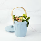 Martha Stewart light blue indoor compost bin filled with vegetable scraps on a marble countertop.