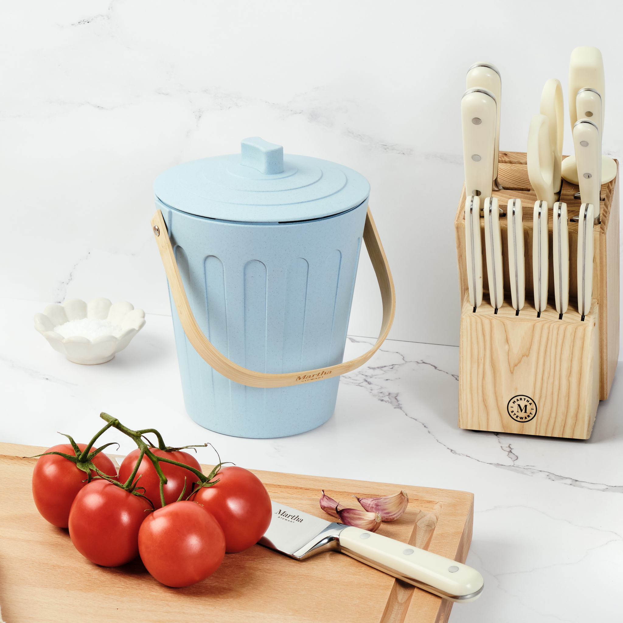 Martha Stewart light blue indoor compost bin next to a wooden cutting board, tomatoes, and a knife block.