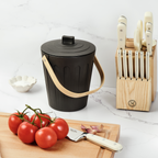 Martha Stewart black indoor compost bin next to a wooden cutting board, tomatoes, and a knife block.