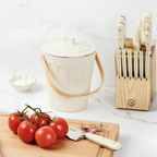Martha Stewart beige indoor compost bin next to a wooden cutting board, tomatoes, and a knife block.