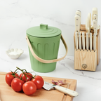 Martha Stewart green indoor compost bin next to a wooden cutting board, tomatoes, and a knife block.
