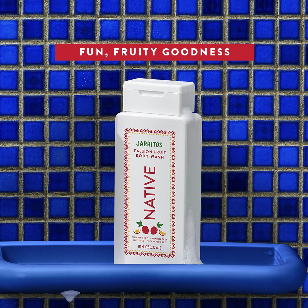 Native Jarritos Passion Fruit body wash bottle covered in suds on a blue tray against blue mosaic shower tiles.