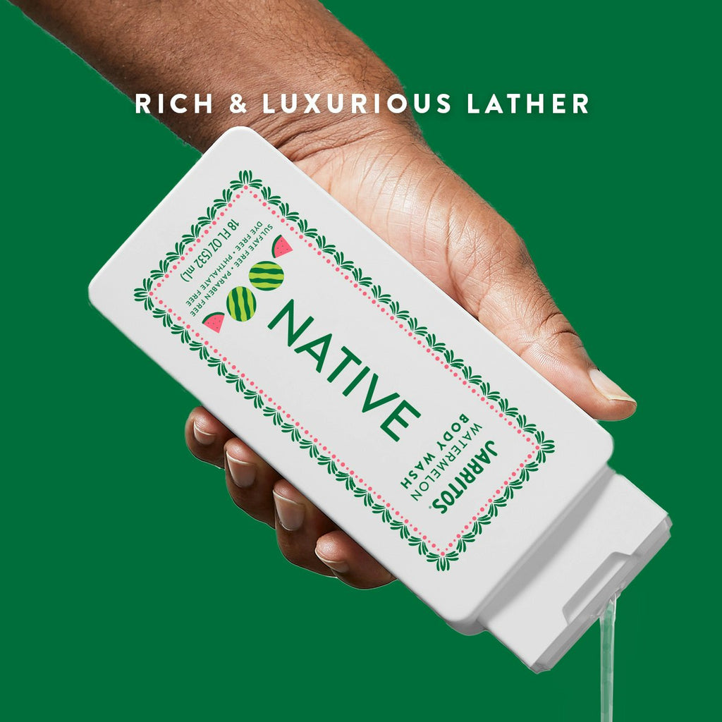 A hand pours clear liquid from a white bottle of Native Jarritos Watermelon body wash over a green background.