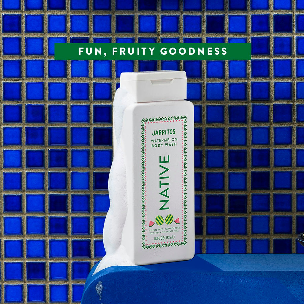 White bottle of Native Jarritos Watermelon body wash covered in lather against a blue tiled shower wall.