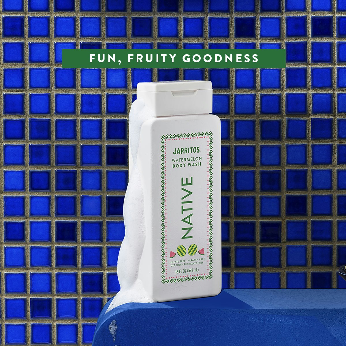 White bottle of Native Jarritos Watermelon body wash covered in lather against a blue tiled shower wall.
