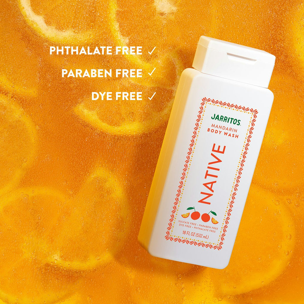 Native Mandarin body wash bottle lying in bubbly orange liquid filled with submerged citrus slices.