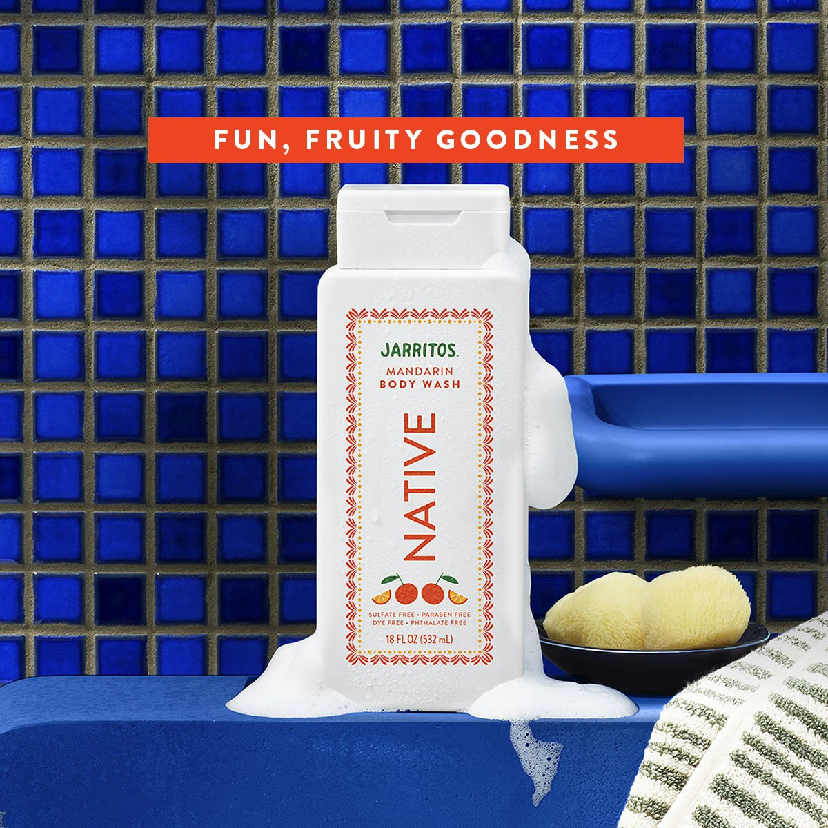 White bottle of Native Mandarin body wash covered in lather on a blue tile shelf beside a bath sponge.
