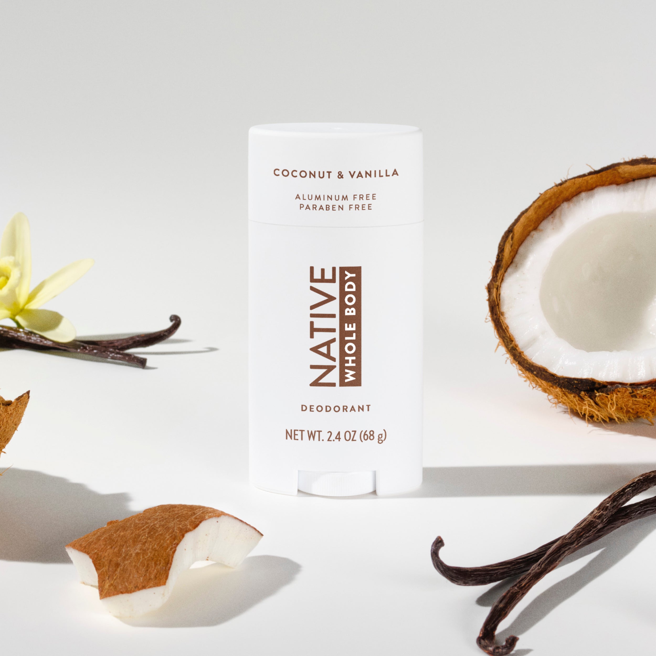 Native Whole Body deodorant stick surrounded by halves of a coconut, a vanilla orchid, and dark vanilla beans.