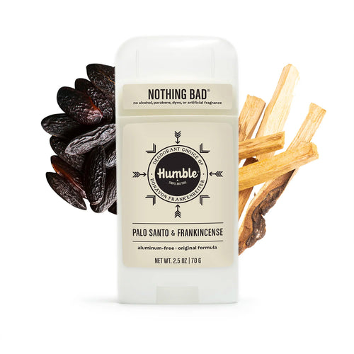 Humble deodorant stick flanked by a pile of dark brown tonka beans on the left and light wood sticks on the right.