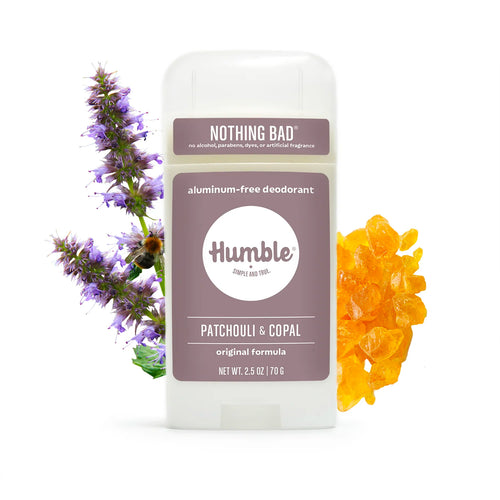 A stick of Humble deodorant flanked by purple patchouli flowers with a bee and golden-orange copal resin chunks.