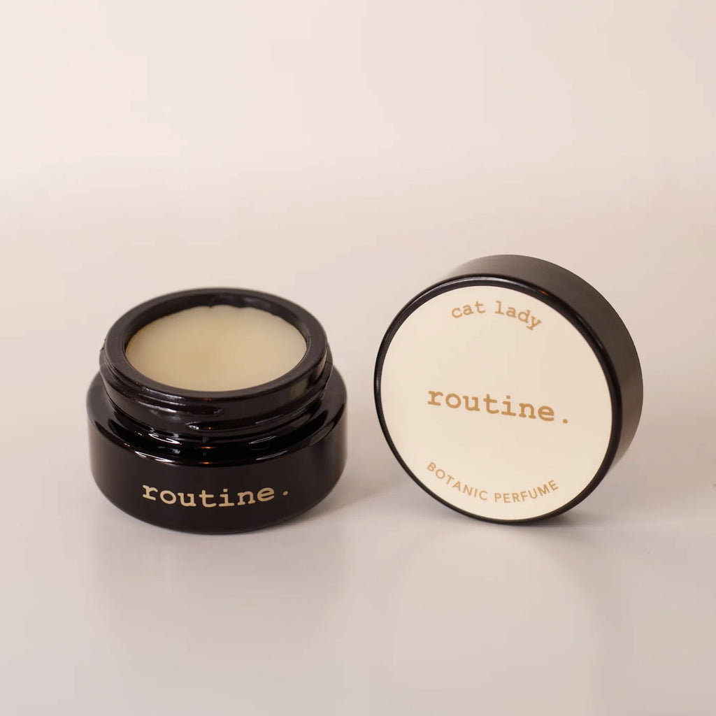 Routine Cat Lady botanic perfume balm - open black glass jar showing cream-coloured solid perfume with detached lid displaying product name - natural moisturizing fragrance balm