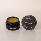 Routine Sexy Sadie botanic perfume balm - open black glass jar showing golden-yellow solid perfume with dark grey lid displaying product name