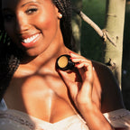 Woman holding Routine Sexy Sadie solid perfume - smiling model holding open black jar showing golden balm in natural sunlight